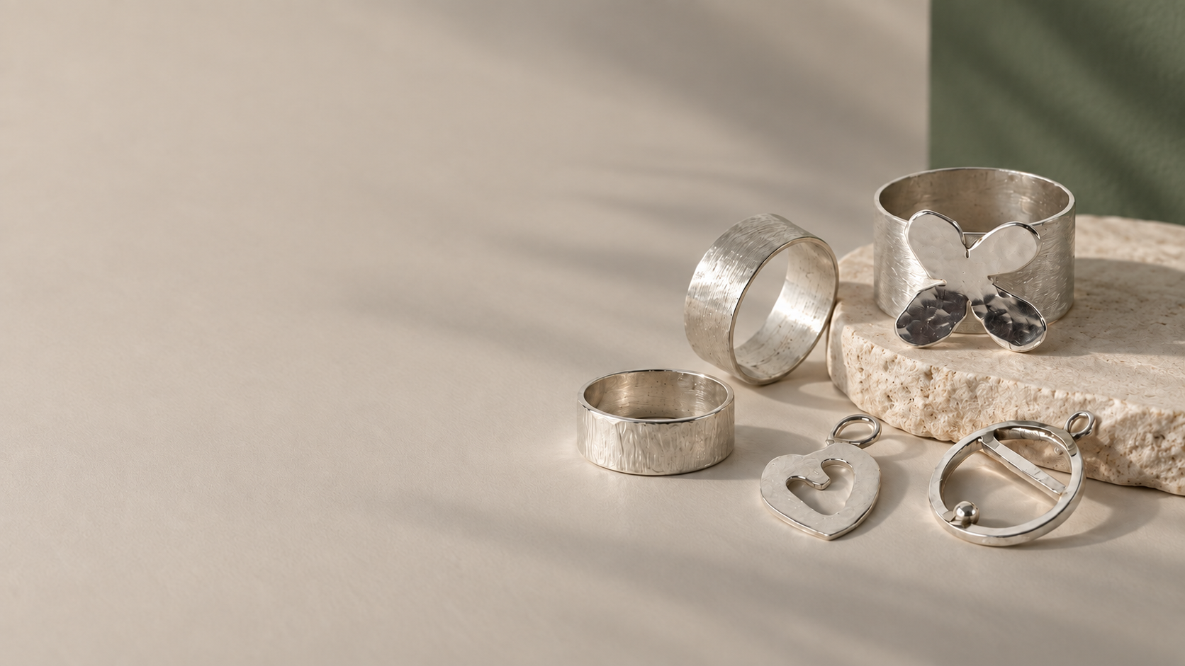Hand-textured silver rings, a butterfly ring and pendants resting on stone